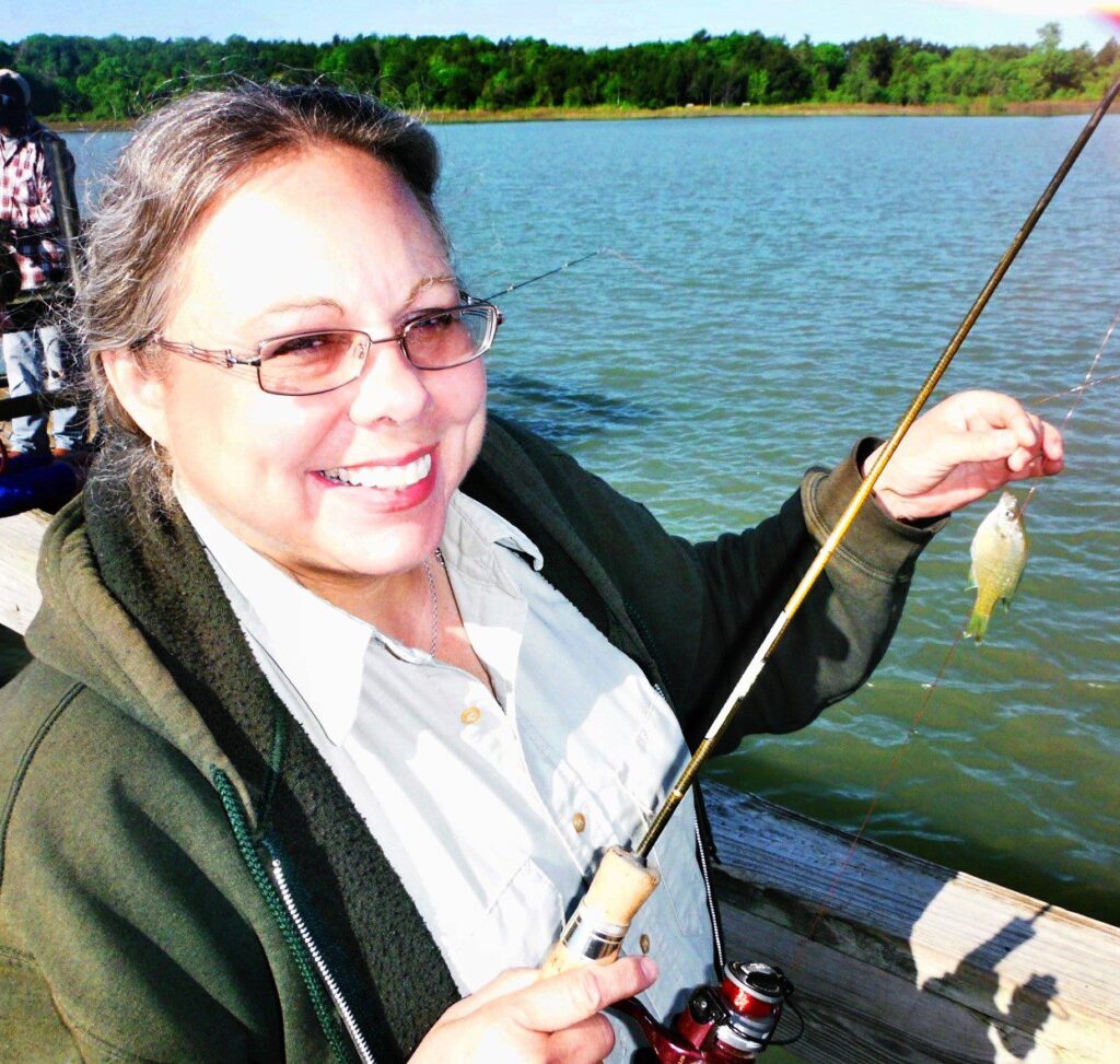 Head and shoulders image of Texas 4-H volunteer Linda Brinlee holding a small fish she caught. 