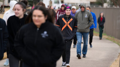 A group of people participating in the Walk Across Texas! program. It is a cold day and they wear jackets and hoods and warm clothing.