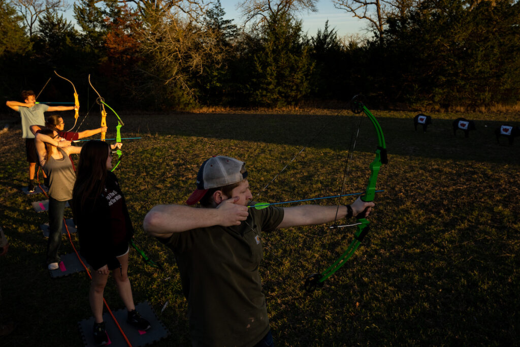Students in a line practice archery outdoors.