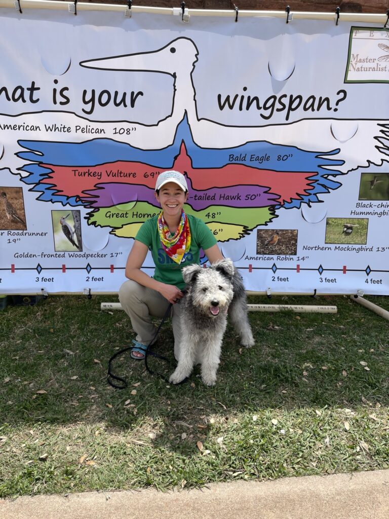 Moore and her herding dog pose in front of a banner with different wingspans depicted at a Master Naturalist event.