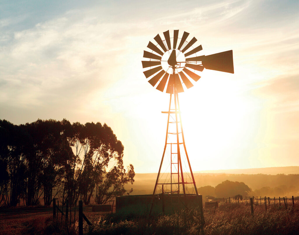 a windmill and water well against a setting sun
