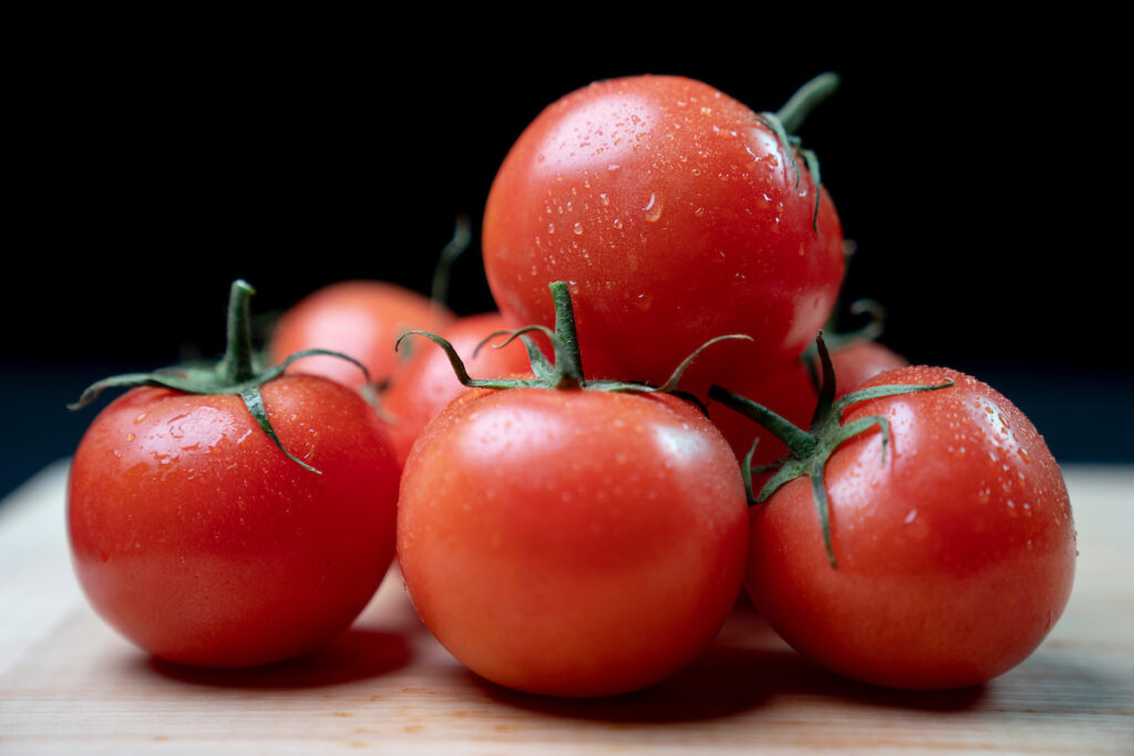 A group of tomatoes is on a table ready for use in cooking a dish.