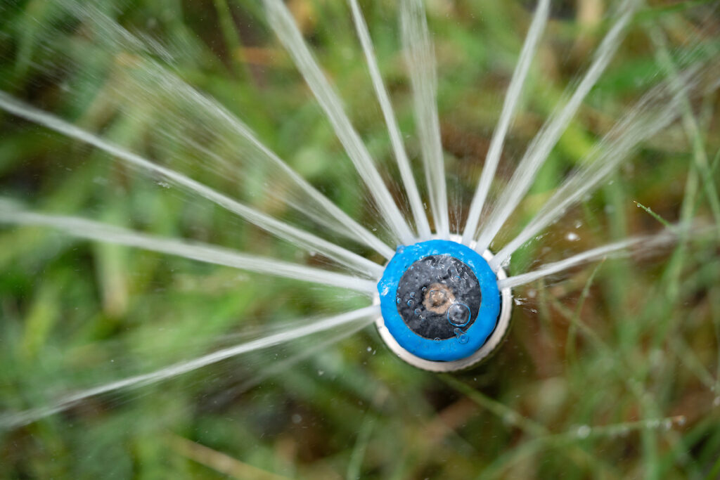 The top view of a blue sprinkler head irrigation system shooting out water in a half-circle at the Gardens at Texas A&M. 