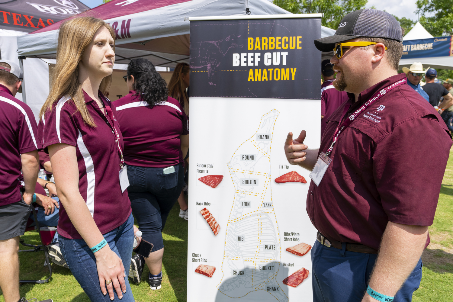 Two Texas A&M students stand in front of a banner displaying Barbecue Beef Cut Anatomy
