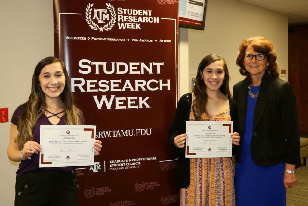 Briana, Bailey Chavez, and Dr. Karen Behrhardt in front of the Student Research Week banner