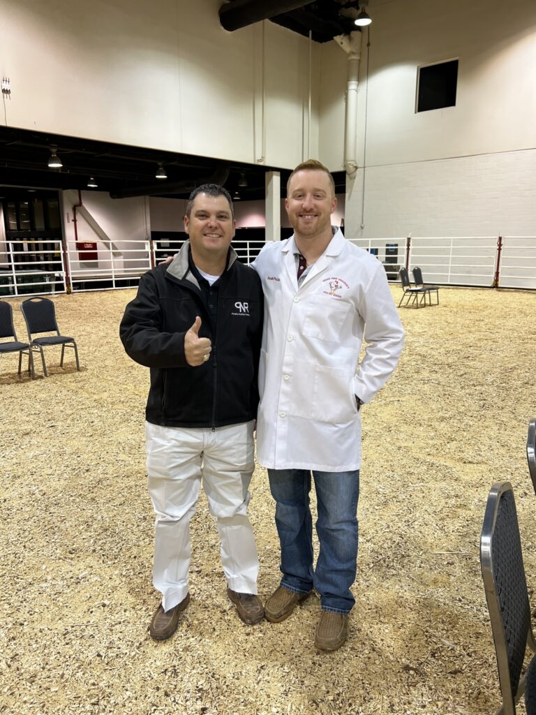 Jason Lee and Jacob Price pose together at a poultry show in a large enclosed arena.