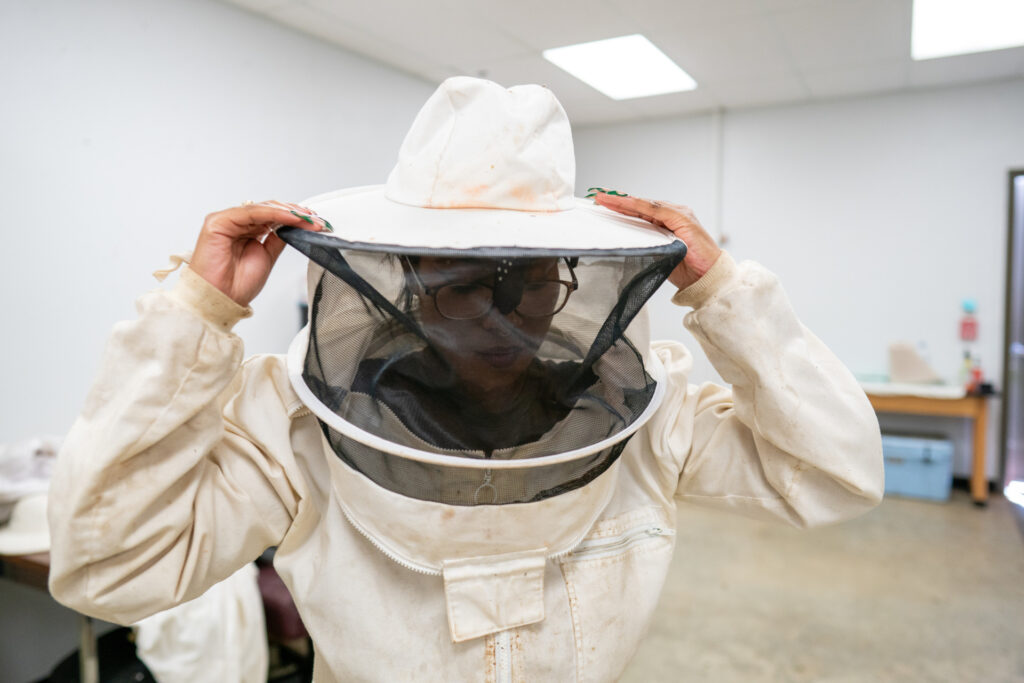 Female student putting on beekeeping hat and gear.