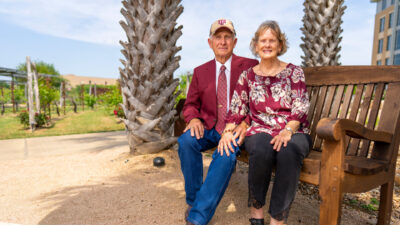 Larry and Pam Leschber sit together on a bench in The Gardens at Texas A&M University, one of the many places they have found joy.