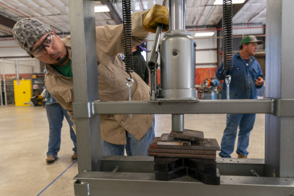 A man using a metal drill press during one of the continuing agricultural education classes .
