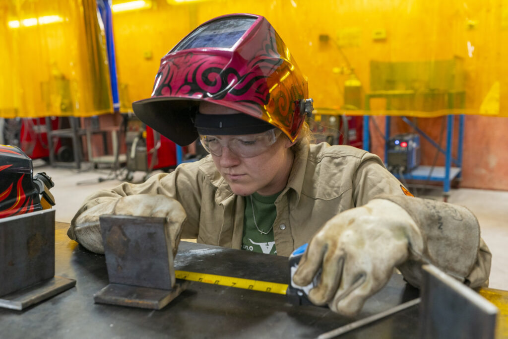 An individual uses a tape measure to measure a piece of steel during one of the continuing agricultural education classes 