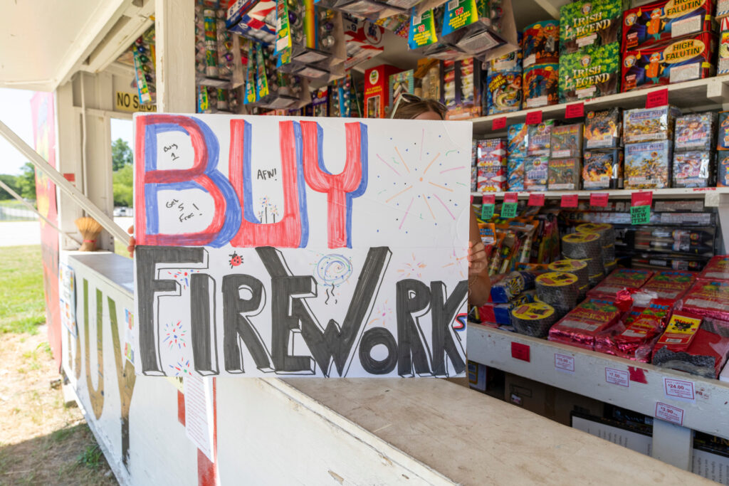 A buy fireworks sign in sits on the counter at a fireworks stand