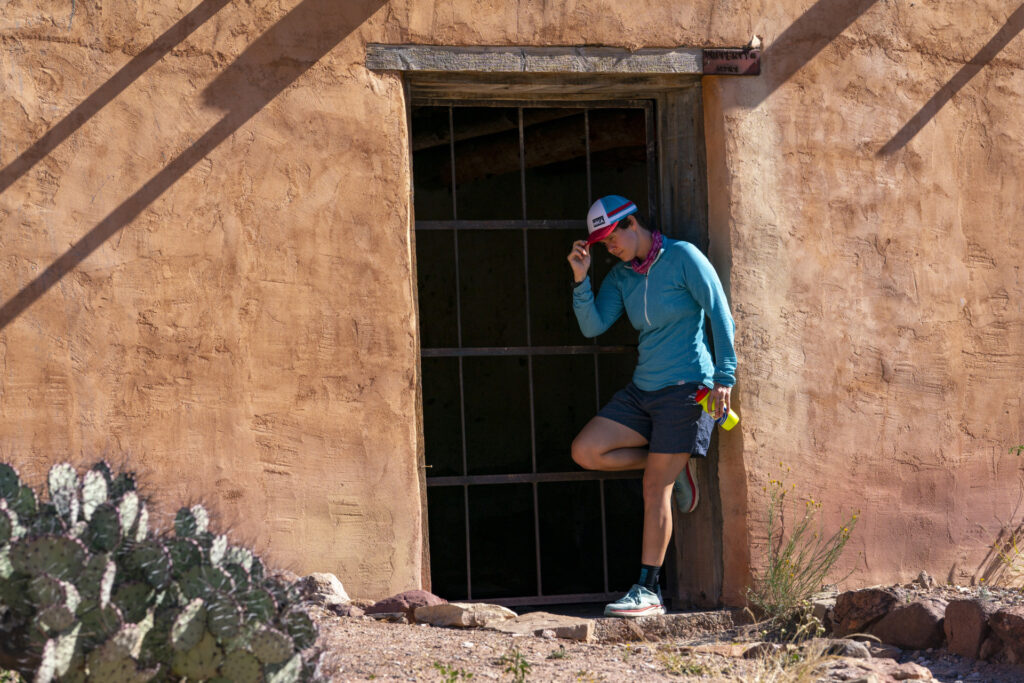 Physically spent young woman in athletic gear in the shaded doorway of an adobe house. Frequent breaks in the shade can help in the prevention of heat stroke.