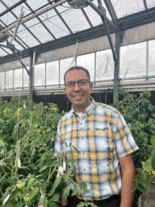 Dr.  Ávila se encuentra entre plantas vegetales en un invernadero. 