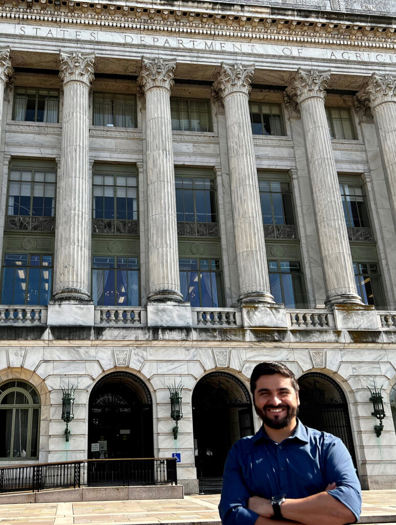 a man, with his arms crossed, standing in front of the USDA building