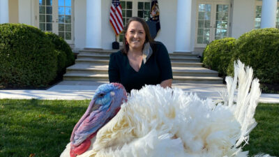 A large white turkey is in the forefront while Leslee Oden kneels behind it on the White House lawn.