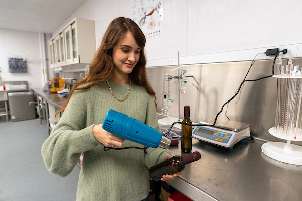 A female student heats the seal of a wine bottle handheld heat shrinker. 
