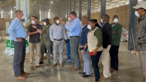 A group of people in safety masks meet in an open warehouse in Botswana with bags of feed on the floor in the background