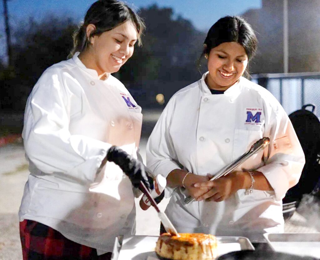 Two women in chef's coats putting dulce de leche on a choco-flan desert.