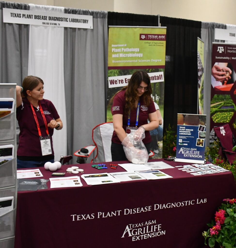 Two ladies from the Texas Plant Disease Diagnostic Lab stand at the lab's booth at the TNLA expo. 