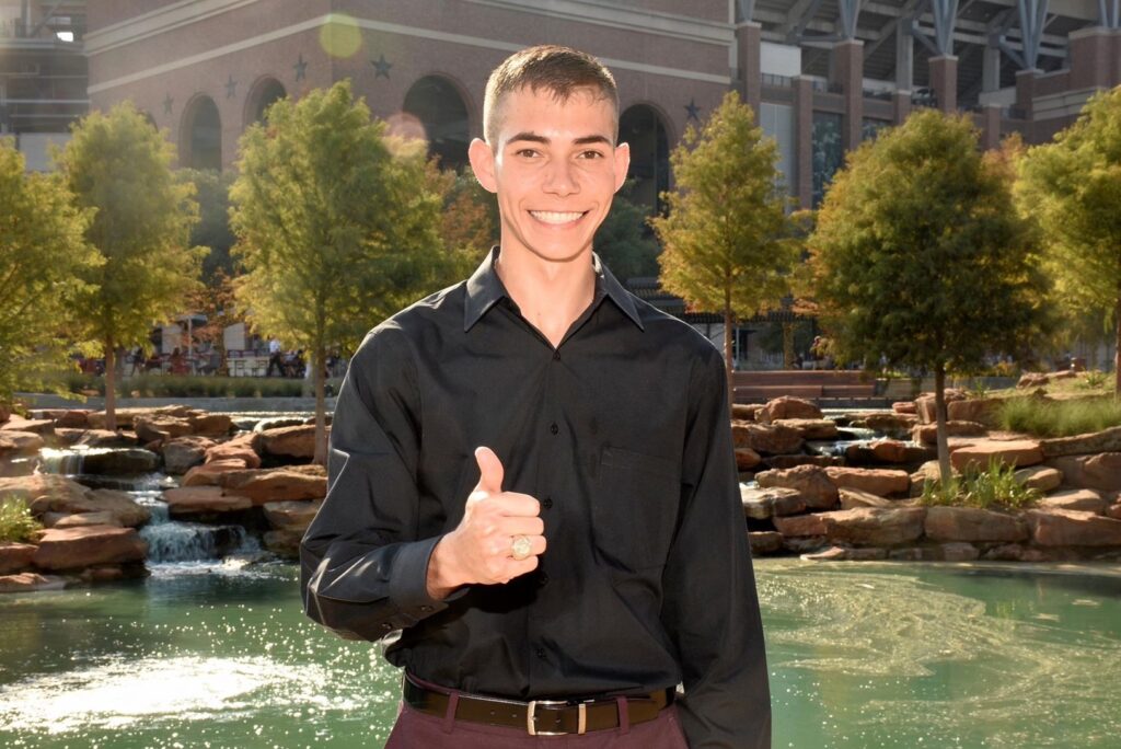 Zane Wanjura, animal science major, in an outdoor setting with his thumb up.