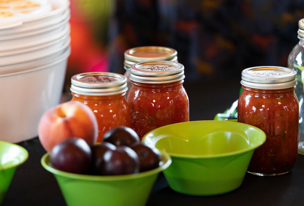Four jars sit on a table behind a bowl of fruit on a table. Participants will learn how to preserve food in jars during a home canning workshop on Oct. 13 in Georgetown.