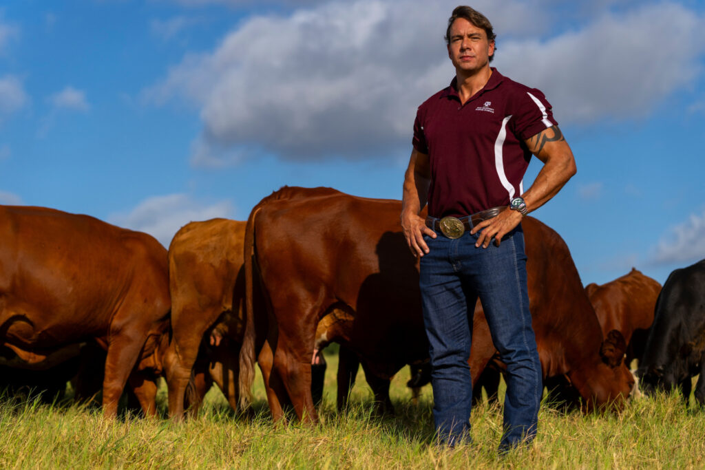 A man standing in a field with beef cattle grazing behind him 