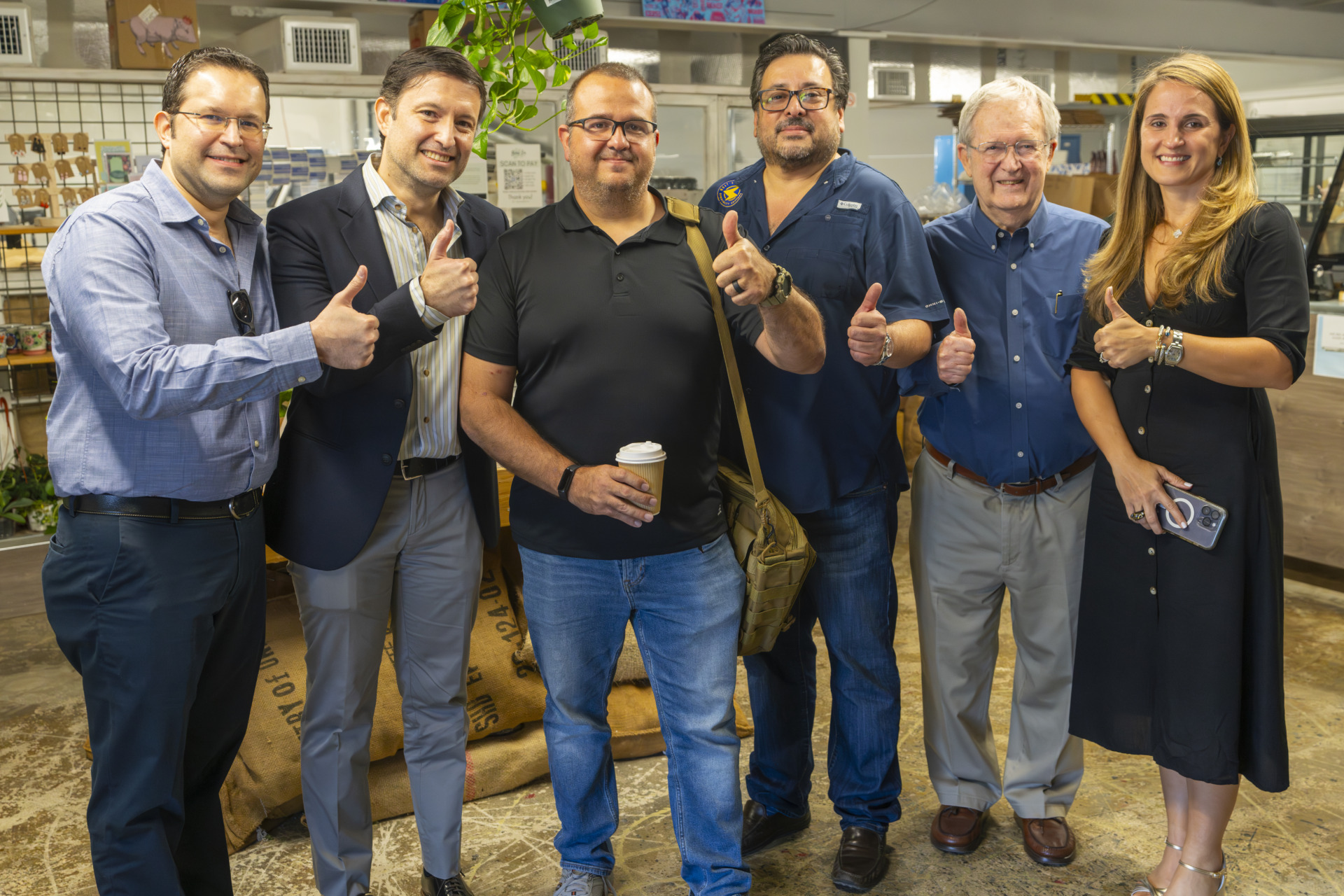 A group of six people, five men and one woman, stands together giving a thumbs up at the launch of the Don Miguel coffee brand, honoring the legacy of the Fernandez siblings father. 