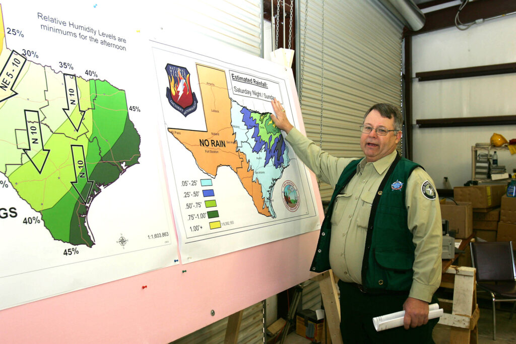 A man, Paul Hannemann, stands in front of several maps that have green shades across them to indicate weather patterns