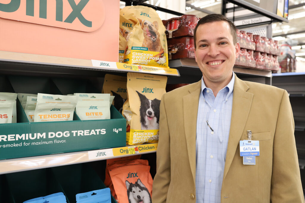 A smiling man, Gatlan Gray, stands in the dog food aisle of a supermarket