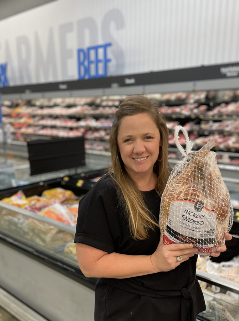 A woman, Rachel Gray, holds a frozen turkey in a supermarket setting.
