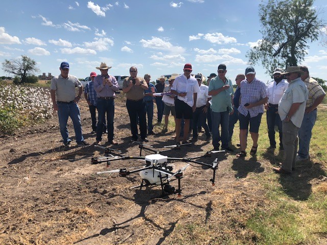 A group of farmers stand around an unmanned aerial vehicle. 
