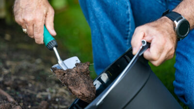 A man's hands are shoveling soil into a bucket.