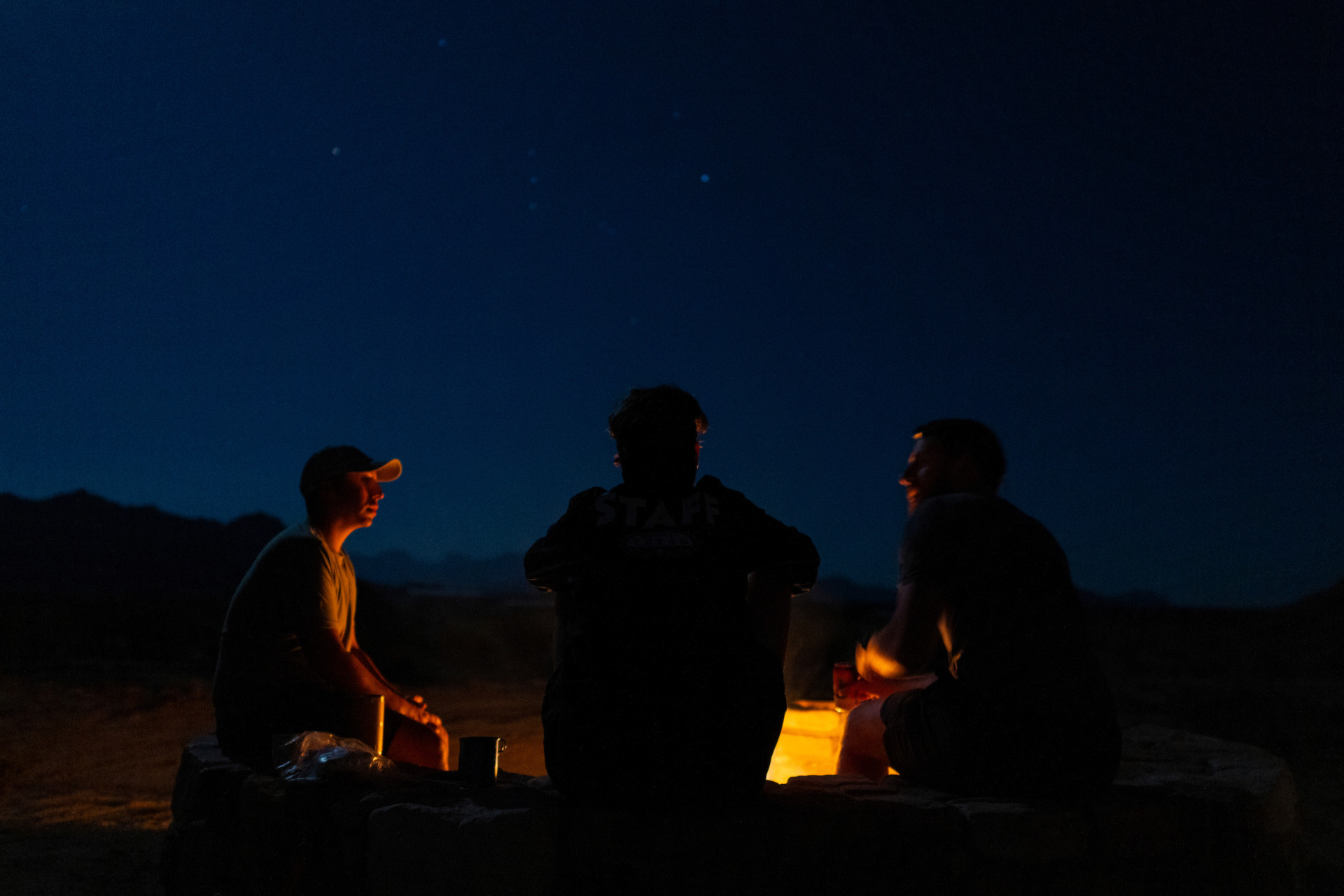 Three people sit around a campfire. 