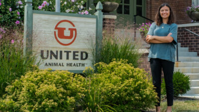 Full body of Camryn Wilder standing in front of a sign that says "United Animal Health".