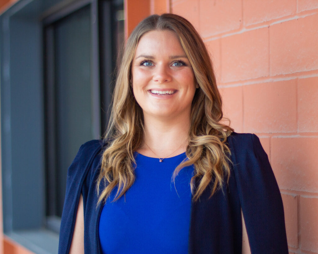A head and shoulders photo of agricultural economics graduate Haley Metteauer. She is wearing a royal blue blouse with a dark blue jacket. 