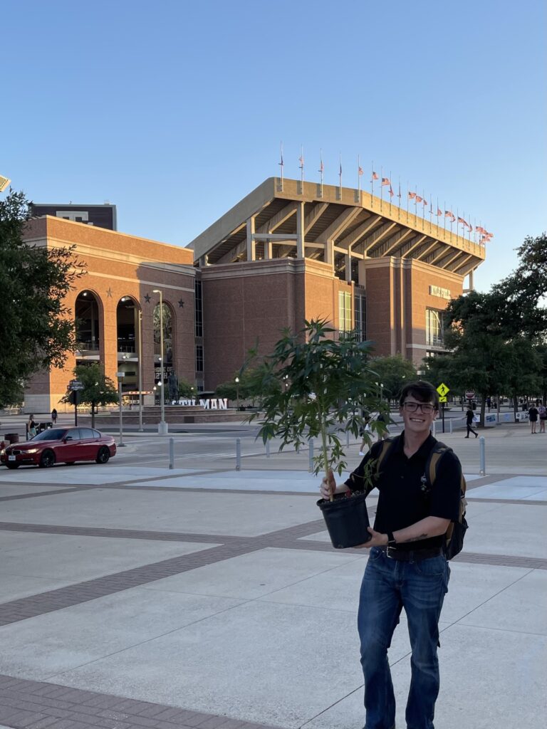 Student Clayton Moore holding a hemp plant in front of Kyle Field at Texas A&M.