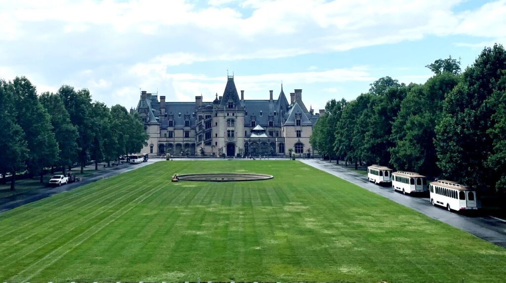 Picture looking at the front of the Inn on Biltmore Estate. There is a green grass area in front with trees lining the drive on both sides. The Inn is among the most prestigious in the hospitality industry