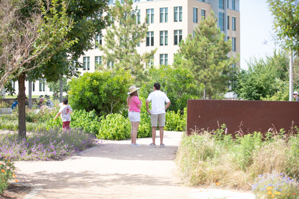 A man and a woman stand in the shade along a path at The Gardens at Texas A&M. 