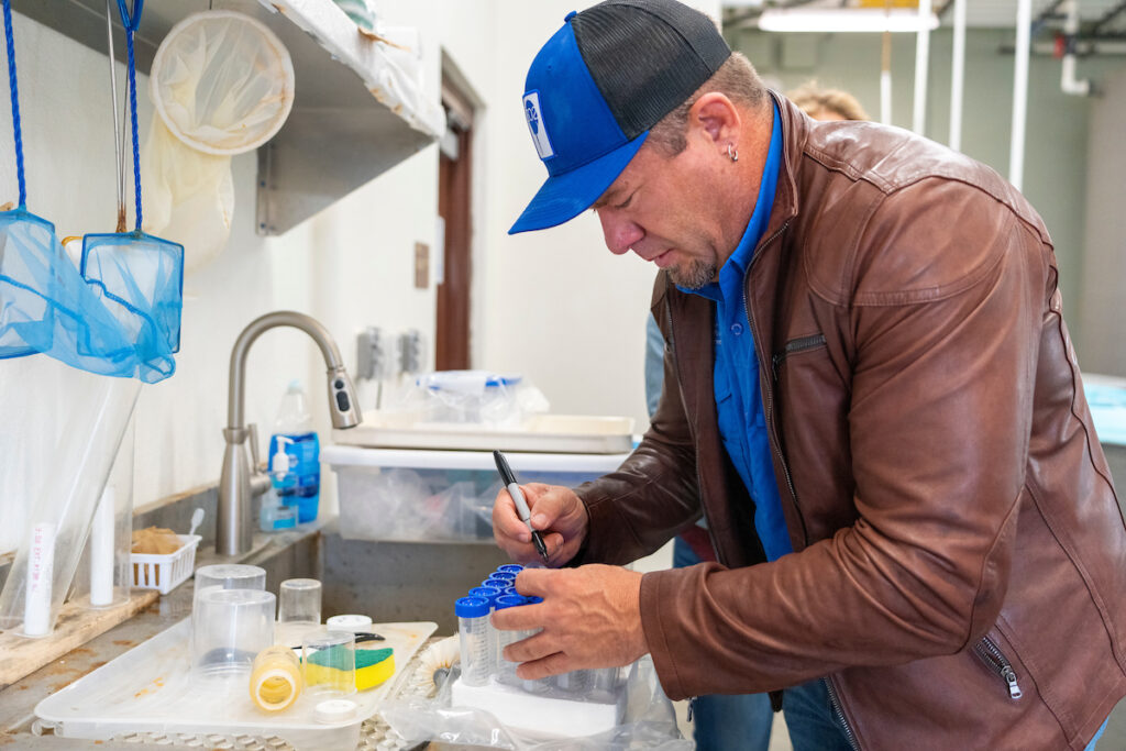 A man wearing a jacket and hat labels tubes in a lab. 