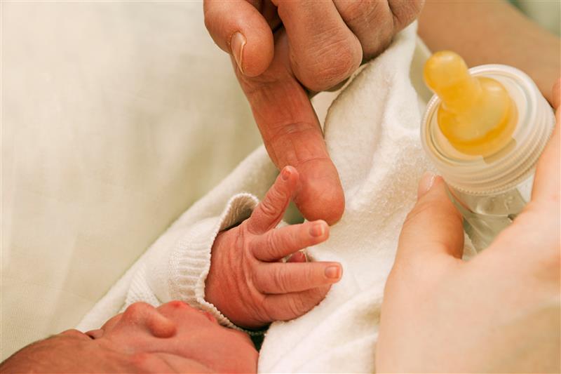 A baby's hand touching the finger of an adult while the adult's other hand holding a baby bottle. Robert Chapkin, Ph.D., is leading an NIH-funded study on feeding intolerance in preterm infants