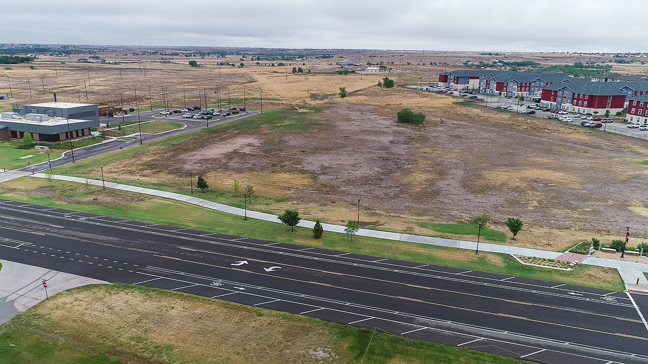 An aerial view looking across a road to an empty field with buildings on one side apartments where construction of the Texas A&M AgriLife Research and Extension Center will take place