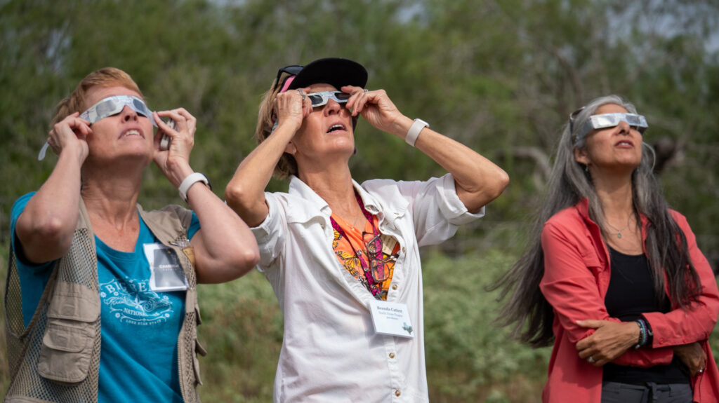 Three women use special glasses to view the 2023 solar eclipse.