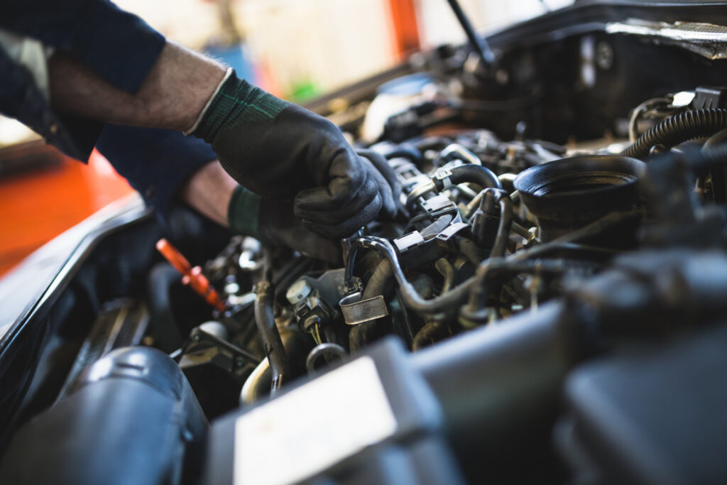Hands wearing mechanic's gloves working on a car engine. Experts suggest getting a tune-up before you travel for the holidays. 