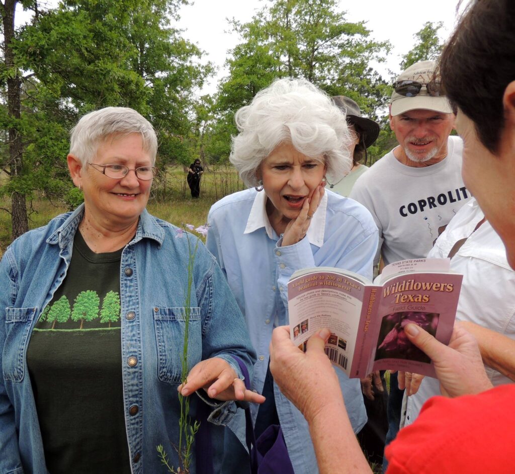 Two women and a man look on as someone shows them an entry from a book titled "Wildflowers of Texas."