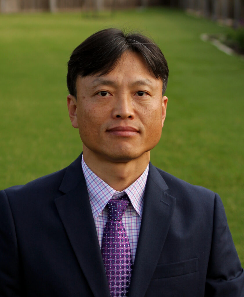 a man, Jaehak Jeong, poses against a green background in his business attire for Regents Fellow picture