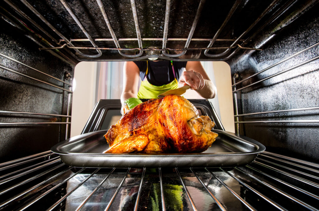 An oven door open with a Thanksgiving turkey inside. A woman is reaching for it.