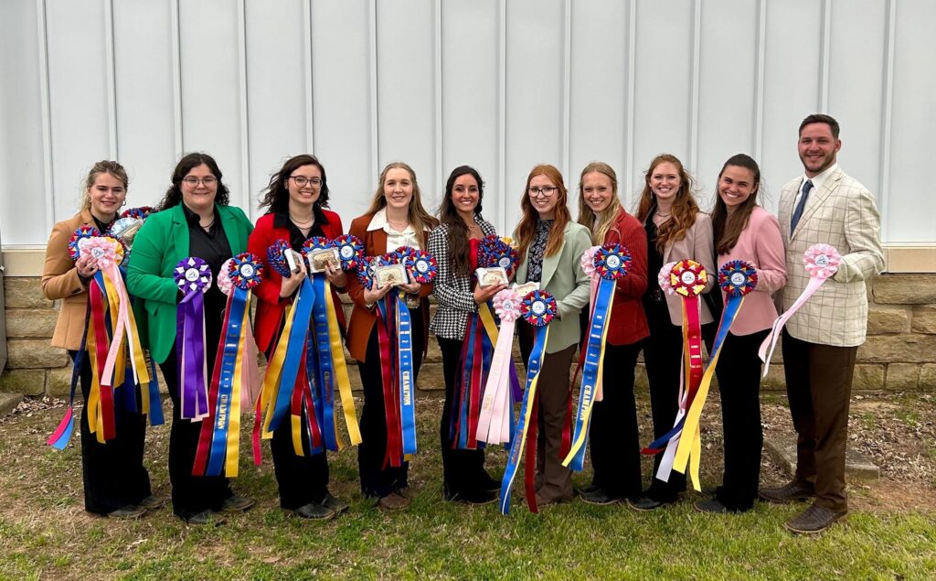 Nine women and one man standing while holding the awards they won. The awards feature a mix of multicolor ribbons.  