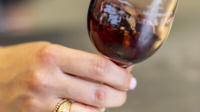 A hand, wearing an Aggie ring, tilts a wine glass