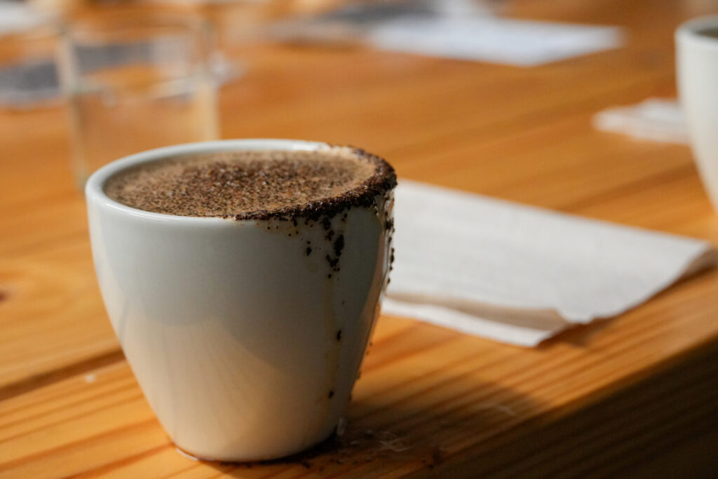 A white cup on a table that holds a dark liquid.