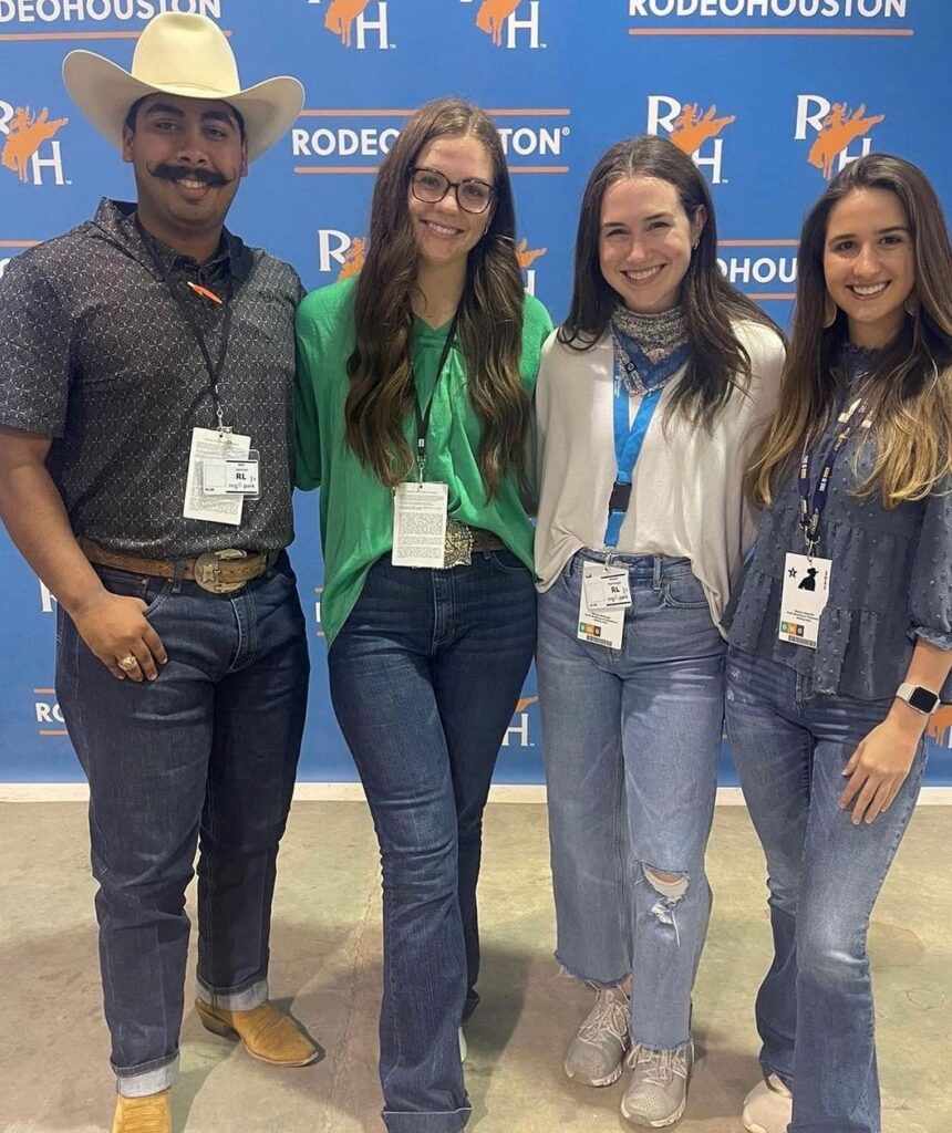 Three women and one man pose at the Houston Livestock Show and Rodeo. They are all part of the internships program and wear press badges